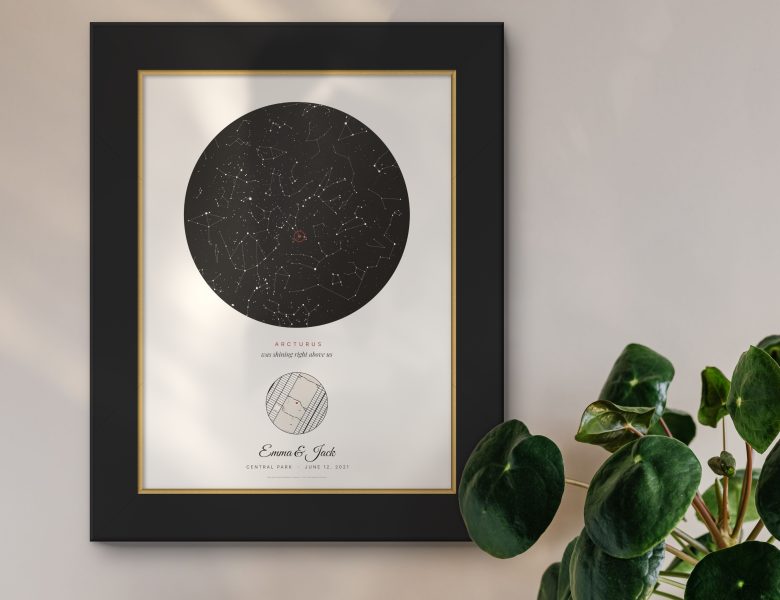 A star map poster in a black and gold frame on a wall, a plant beside it