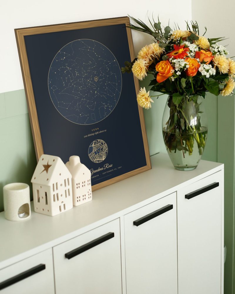 A navy star map poster in an oak frame on a sideboard with flowers