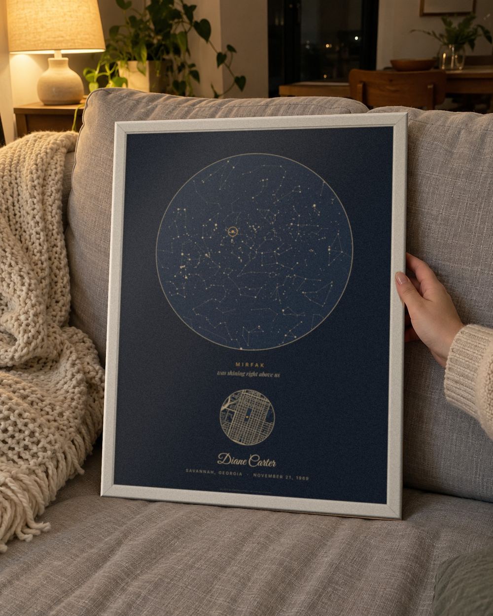 Birthday star map in a white frame held on a sofa, an example: Our star design in Navy, Savannah, Georgia, November 21, 1969, Mirfak circled, name Diane Carter