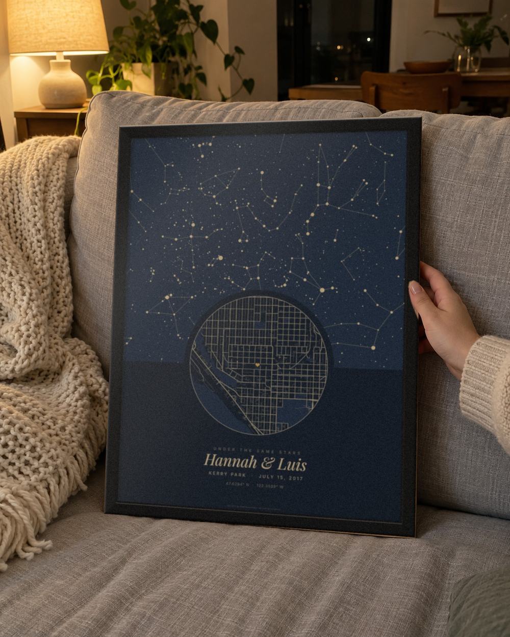 First kiss map in a black frame held on a sofa, an example: Under the stars in Navy for Kerry Park, Seattle, July 15, 2017, that night's sky over the streets of Queen Anne, the heart on the viewpoint, names Hannah & Luis