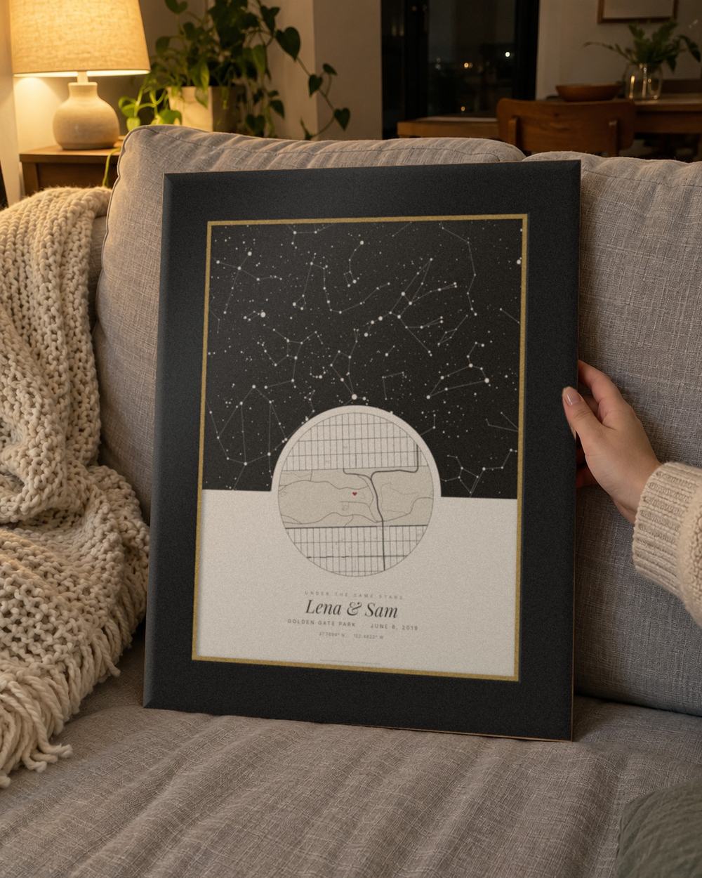 Star map gift in a black and gold frame held on a sofa, an example: Under the same stars design in Cream, Golden Gate Park, San Francisco, June 8, 2019, names Lena & Sam